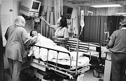 Nurses caring for a patient who is in a hospital bed. One nurse is checking a monitor.
