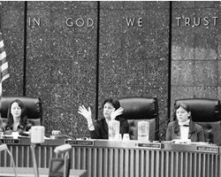 Dion Aroner jestruing, with aids on either side. Seated in the council chambers 