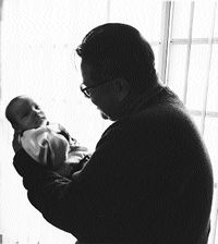 social worker holding a baby siloueted next to a window-the  size of the social worker's head and concerned look compared to the baby's  small head and  smile gie a very warm feeling