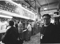 Jacob Ocampo in a public market place near a food stand, wiht a check cashing sign behind him. He is hoping to find  parents to speak with  who need information about child welfare.