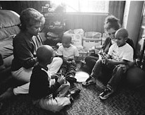 Adoptions worker with a family. They room is filed with children and the worker and mother are playing with the kids.