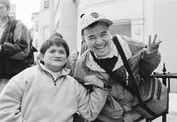 Two people with disablities  smiling and gesturing at the camera