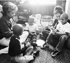 Amy and the family sitting in the den. One of the children is sitting on Amy's lap showing her a toy.