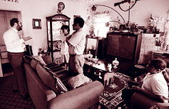 Social worker making a home visit. He is explaining something to a family. They are in a living room with a couch, large TV and other nice furnature. Obviously a working family that is doing  well. They are hispanic.