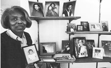 Jackson holding up a photograph of her grand daughter. There are several sheleves of family photos in the background.
