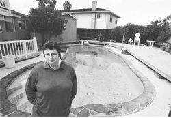 Maryellen standing in her backyard with a swiming pool in the background, the scene looks very suburban and lonely.