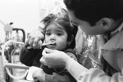 Child in dental chair with dentist holding the tooth brush, child looks nervious, mother watches