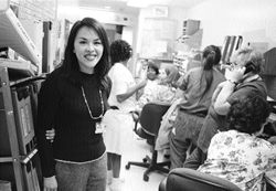 An Nguren, standing in teh office with people on teh phone and nurses in scrubs talking.