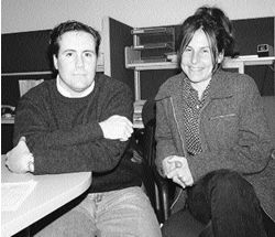 Jason and Pam sitting and talking to camera, Jason is wearing a sweater, Pam has a light jacket on and her hair is up. She has a very large and warm smile