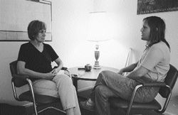 Therapy scession with Peggy listening to Shara. Sitting by a lamp table, facing each other.