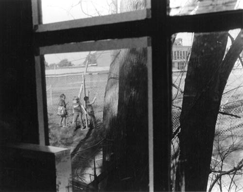 three kids walking next to a fence seen through a window